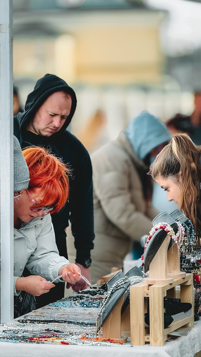 A group of people browsing jewelry at an outdoor market stall on a chilly day.